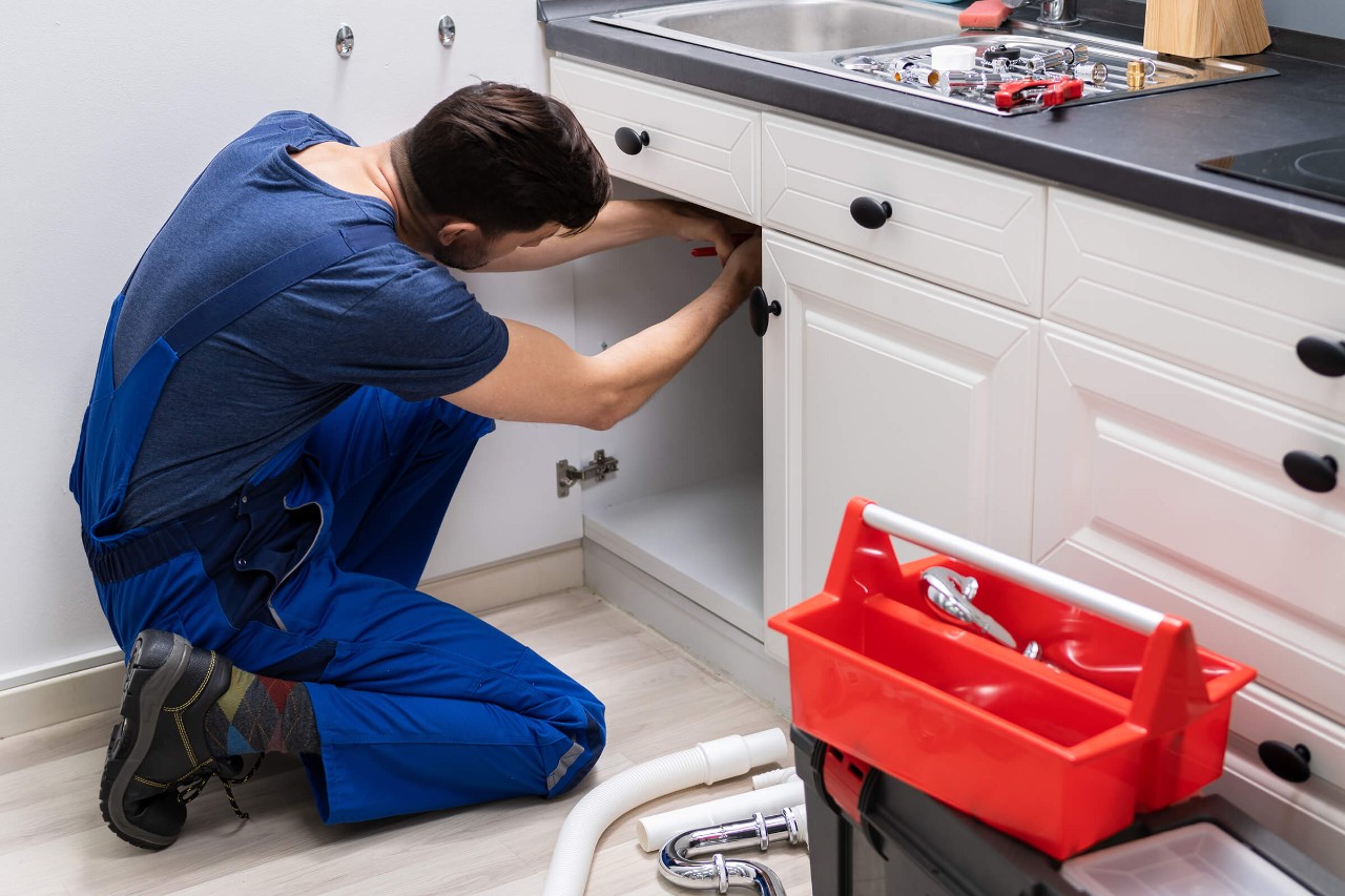 rørlegger installerer vannstopper under kjøkkenvasken i et hus