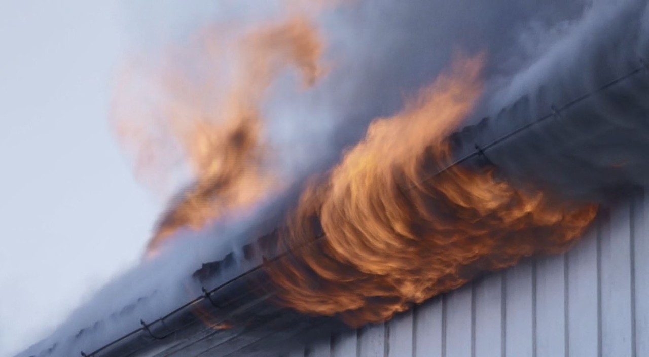 husbrann der flammene kommer ut av taket på et hus