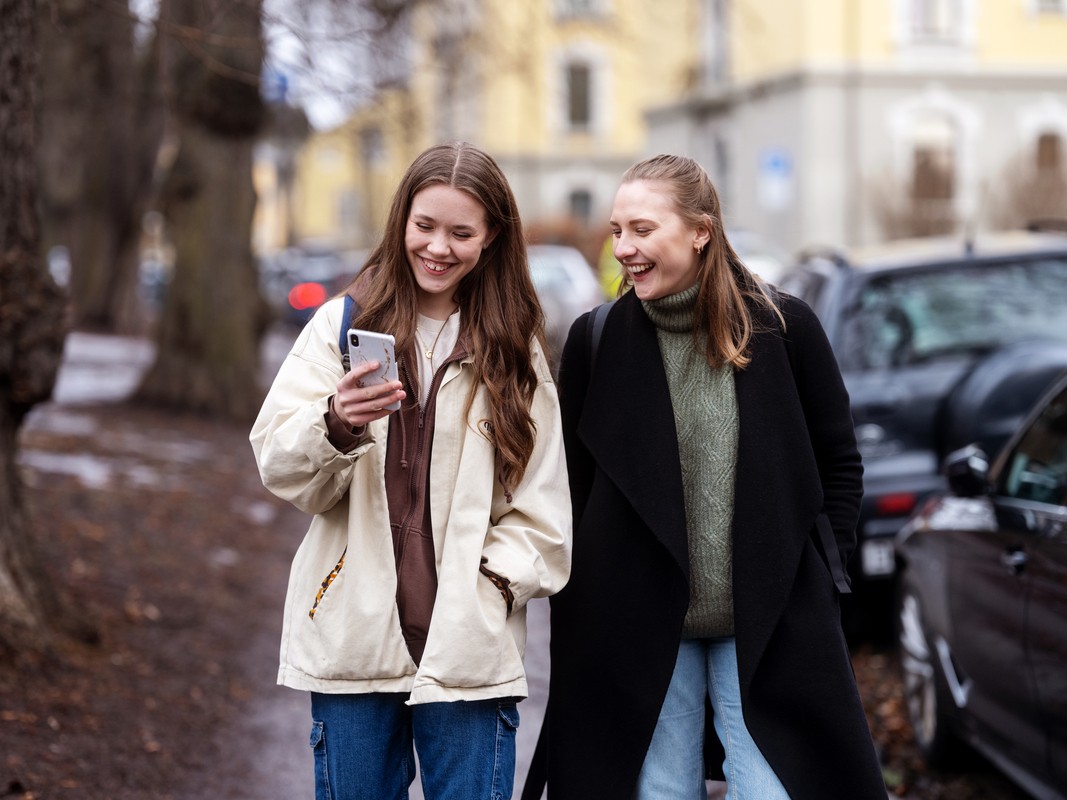 To smilende jenter ser på mobilen som hun ene holder