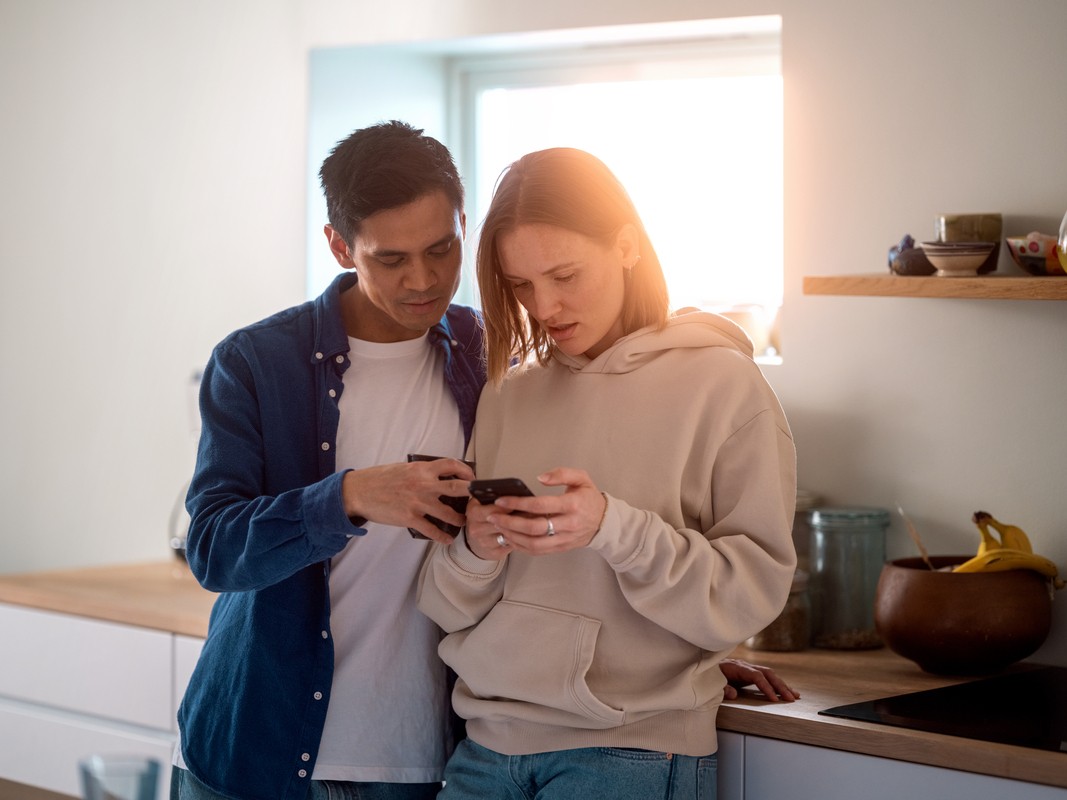 En mann og en dame står ved en kjøkkenbenk og ser på en mobil