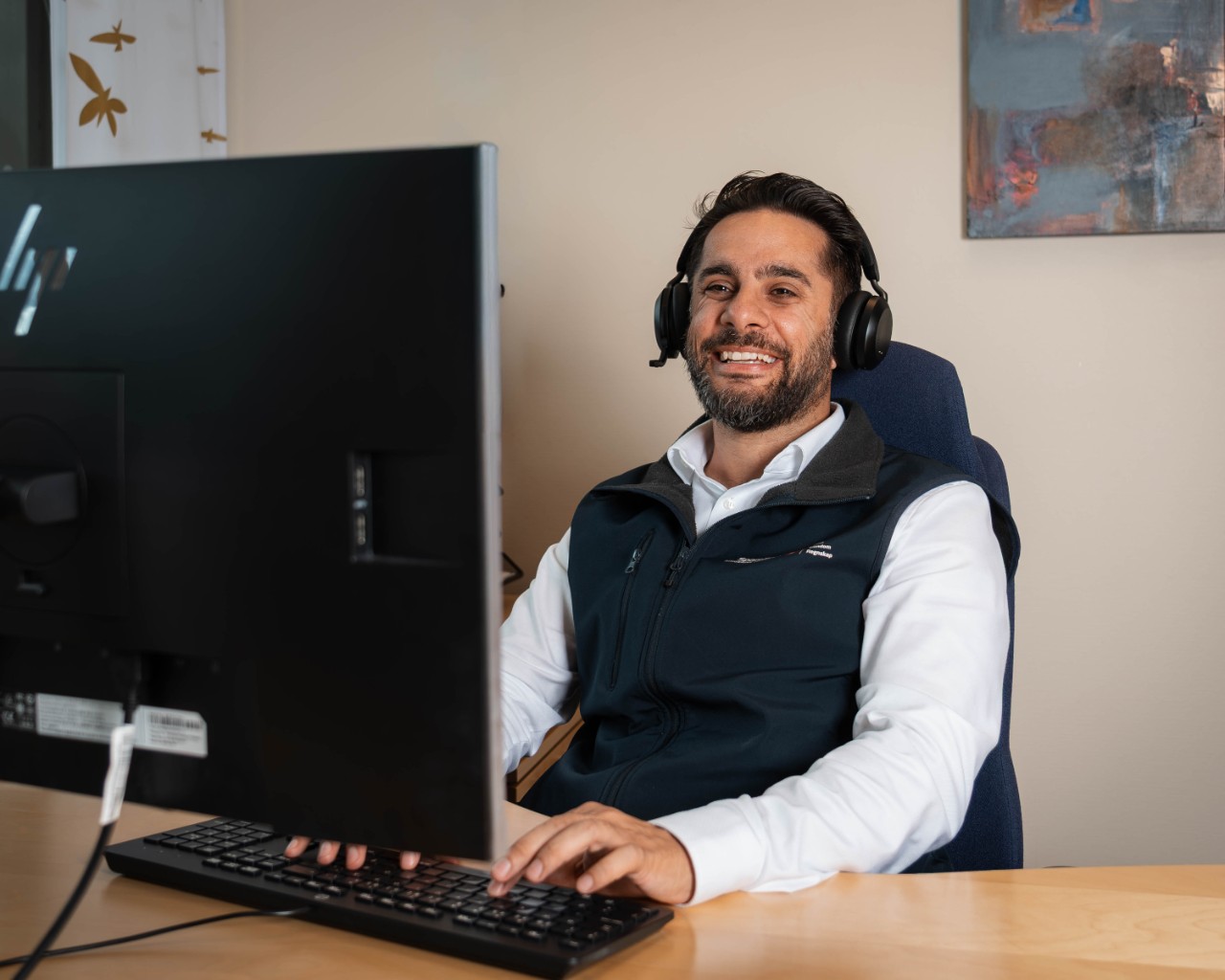 Rådgiver personmarked Shovan med headset på, smilende i samtale med kunde digitalt.