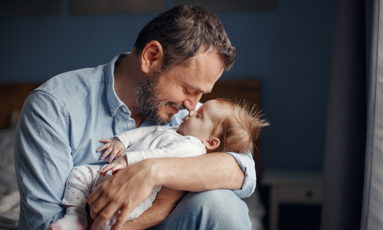Middle age Caucasian father kissing sleeping newborn baby girl. Parent holding rocking child daughter son in hands. Authentic lifestyle parenting fatherhood moment. Single dad family home life.