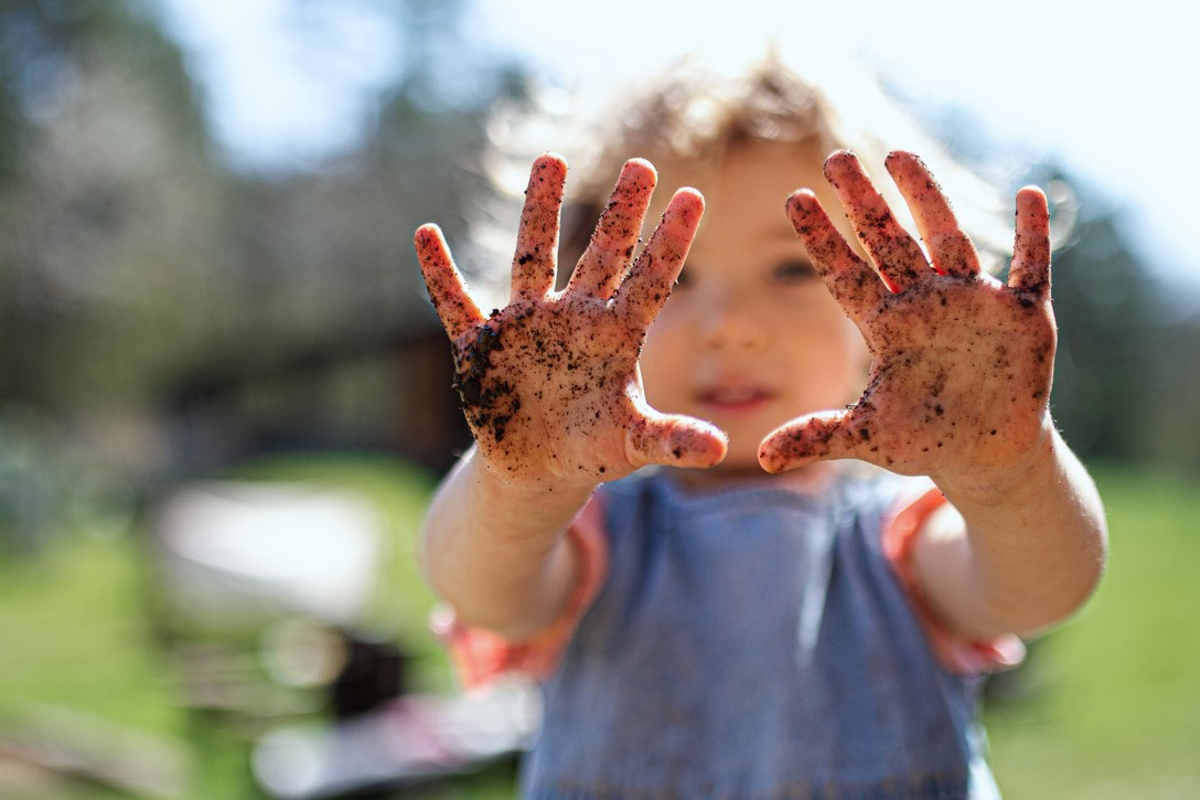 Portrait of small girl showing dirty hands outdoors in garden, sustainable lifestyle concept.