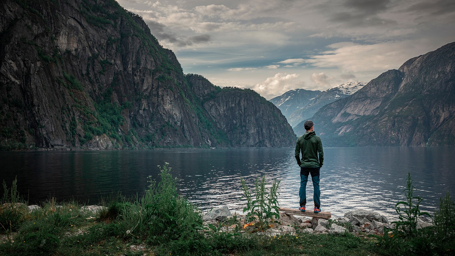 Man standing at waterfront of lake in the mountain landscape Eidfjord in Norway, looking into the fjord, clouds in the sky