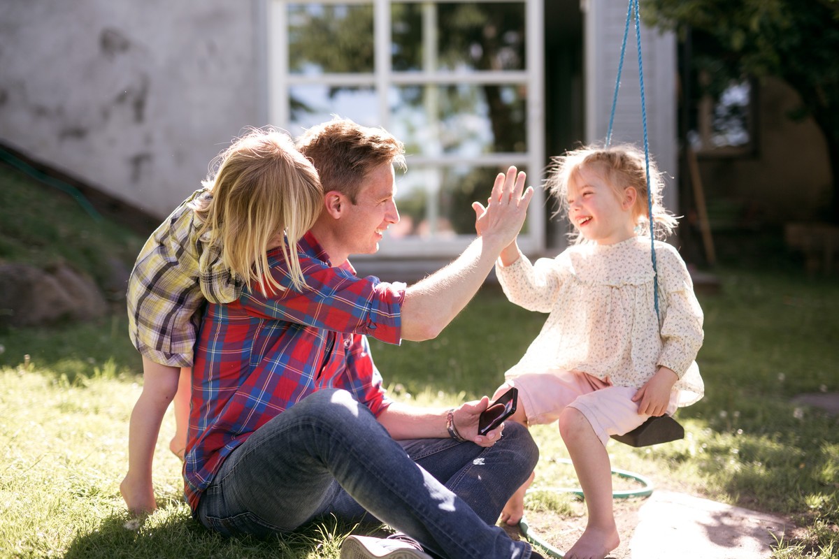 liten familie med far og to døtre leker i hagen en solskinnsdag