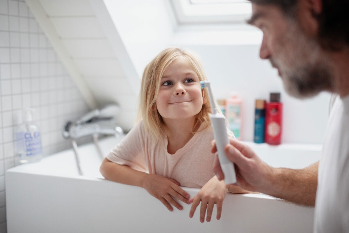 far med gruppelivsforsikring via jobben sin hjelper datteren med å pusse tennene på badet