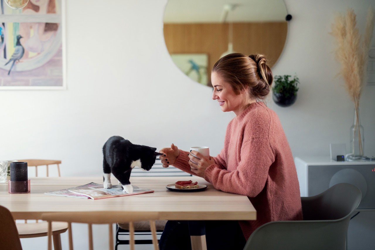 Ung kvinne spiser med katt på bordet