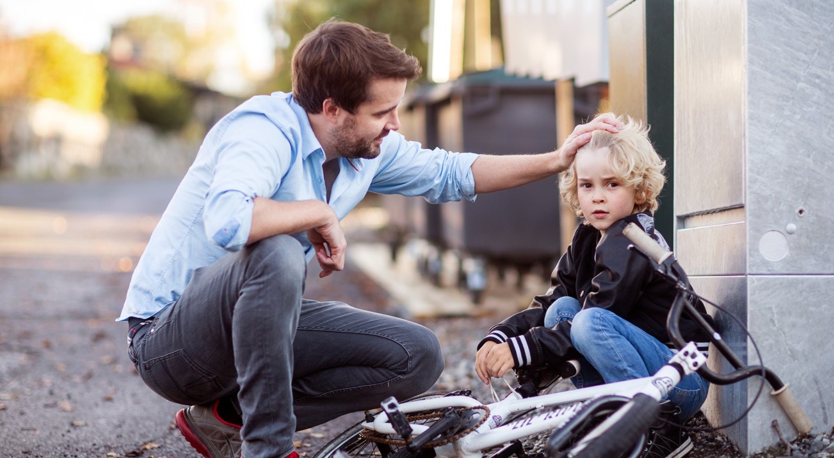 Far (som vet hvilke forsikringer bør man ha) trøster sønn som har falt av sykkelen sin.