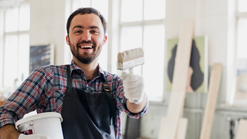 Maler med enkeltpersonforetak smiler og holder opp malerkosten mot kamera
