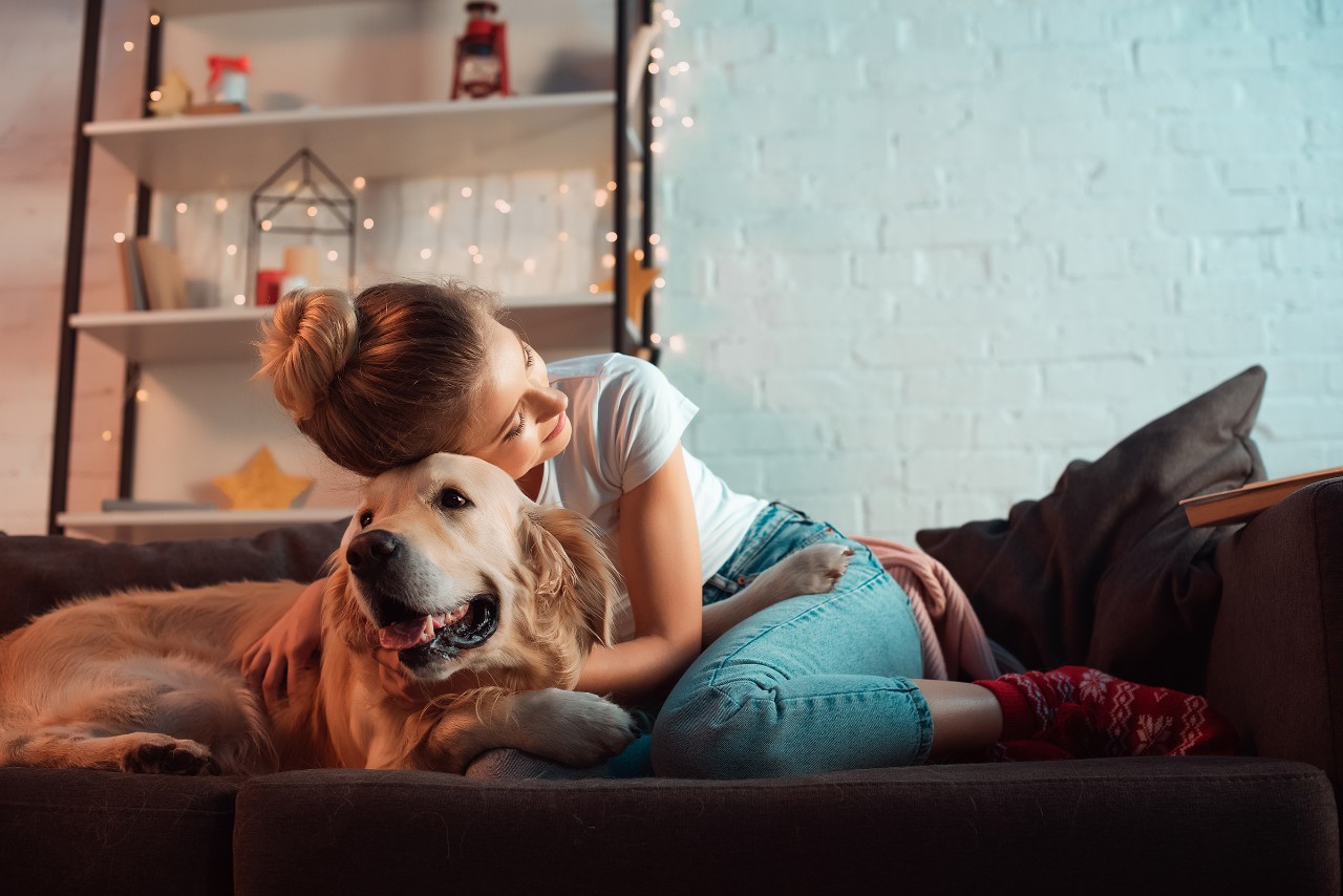 Ung dame på sofa koser med Golden Retriever, julestemning