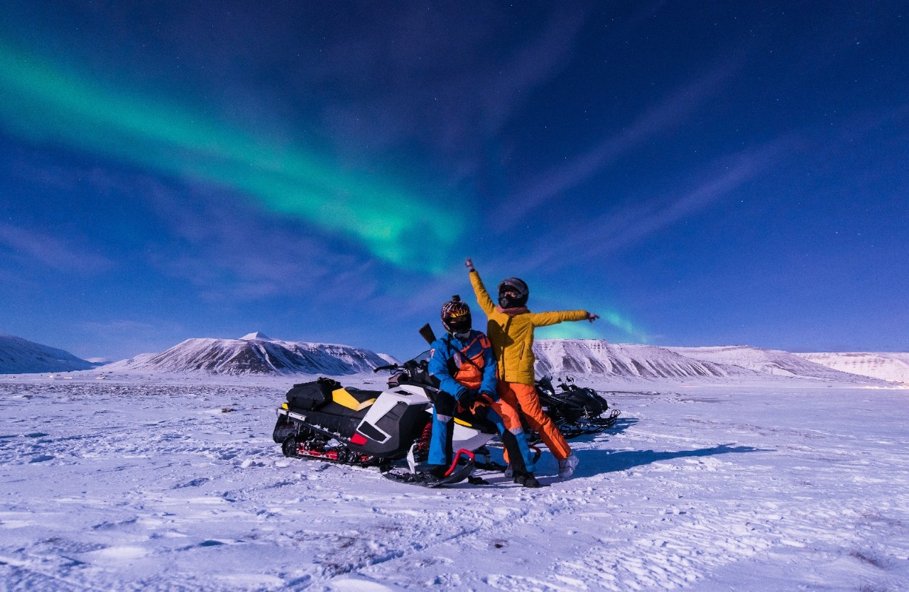 Par på snøscooter i nordlys. Foto.