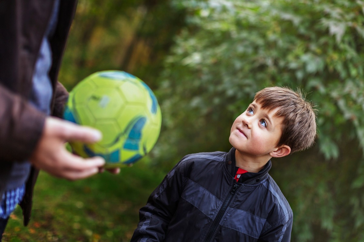 fotboll i förgrund, pojke tittar upp på person