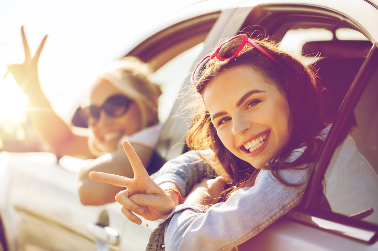 Jenter med delkasko i bil viser peace-tegn med fingrene ut av ruta