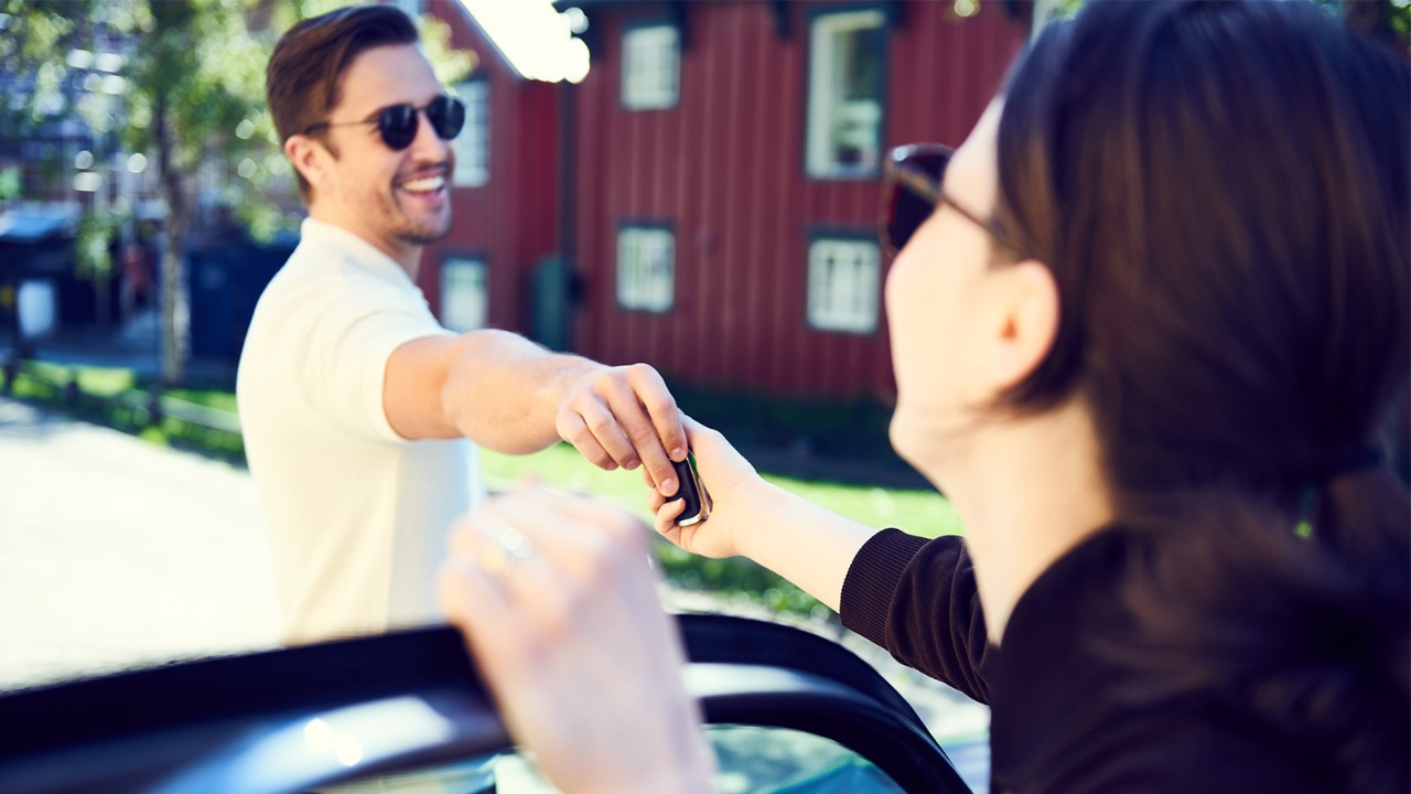 Smilende mann gir bilnøkkel til kvinne. Foto.