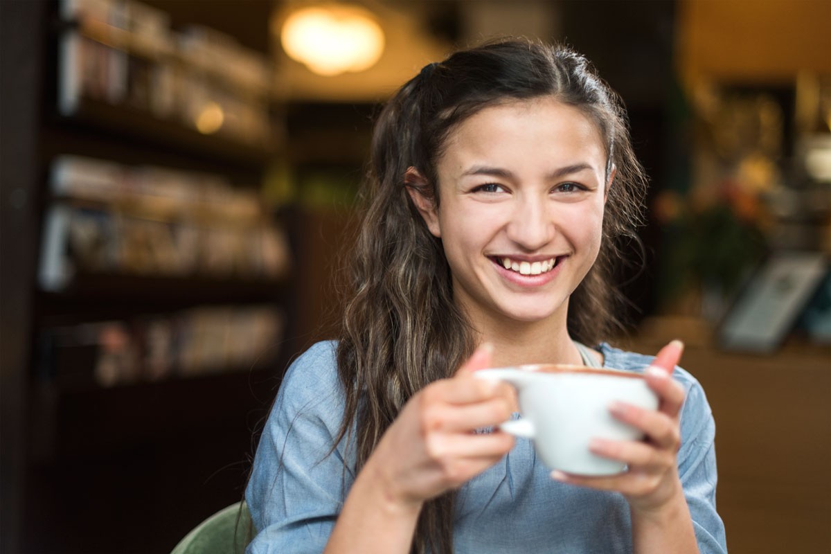 Blid jente sitter på kafe med kaffekopp