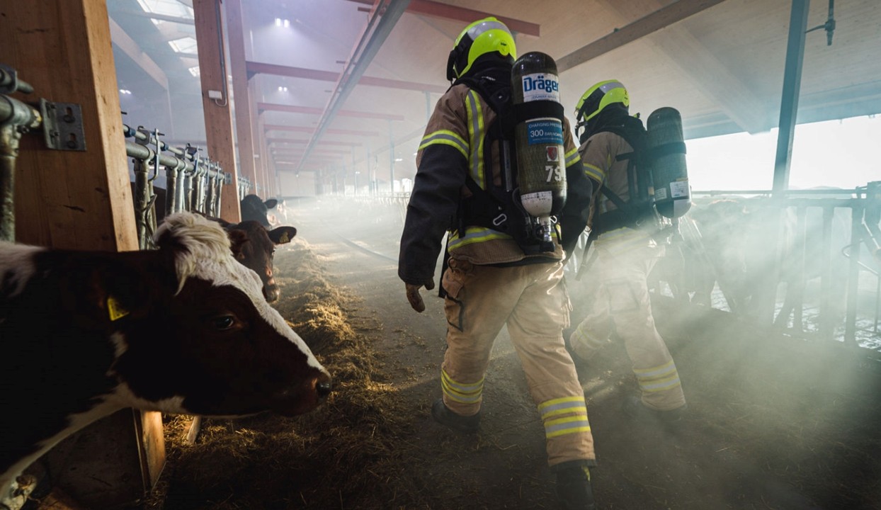landbruksdriftsbygning i brann og brannmann som jobber med å slukke