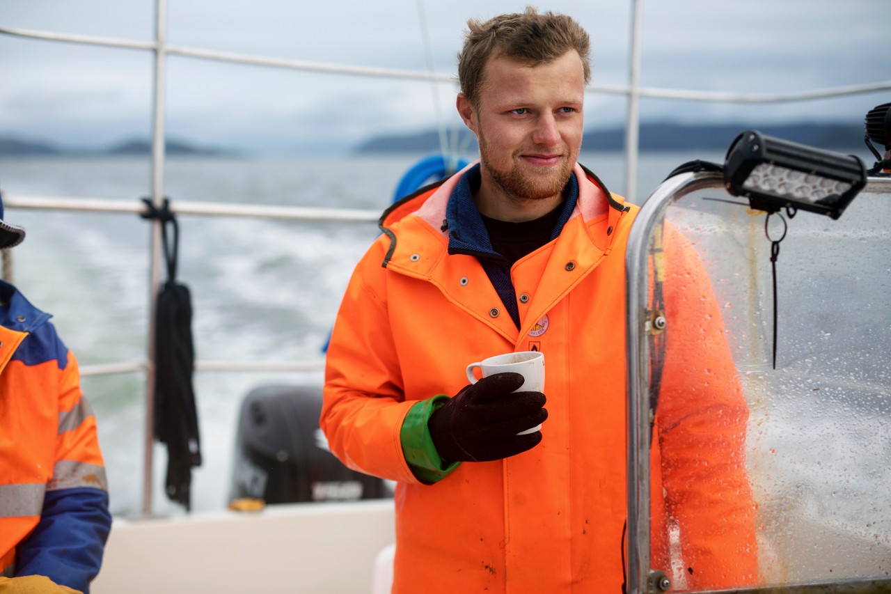 selvstendig næringsdrivende fisker står med kaffekopp i hånda og titter utover fjorden