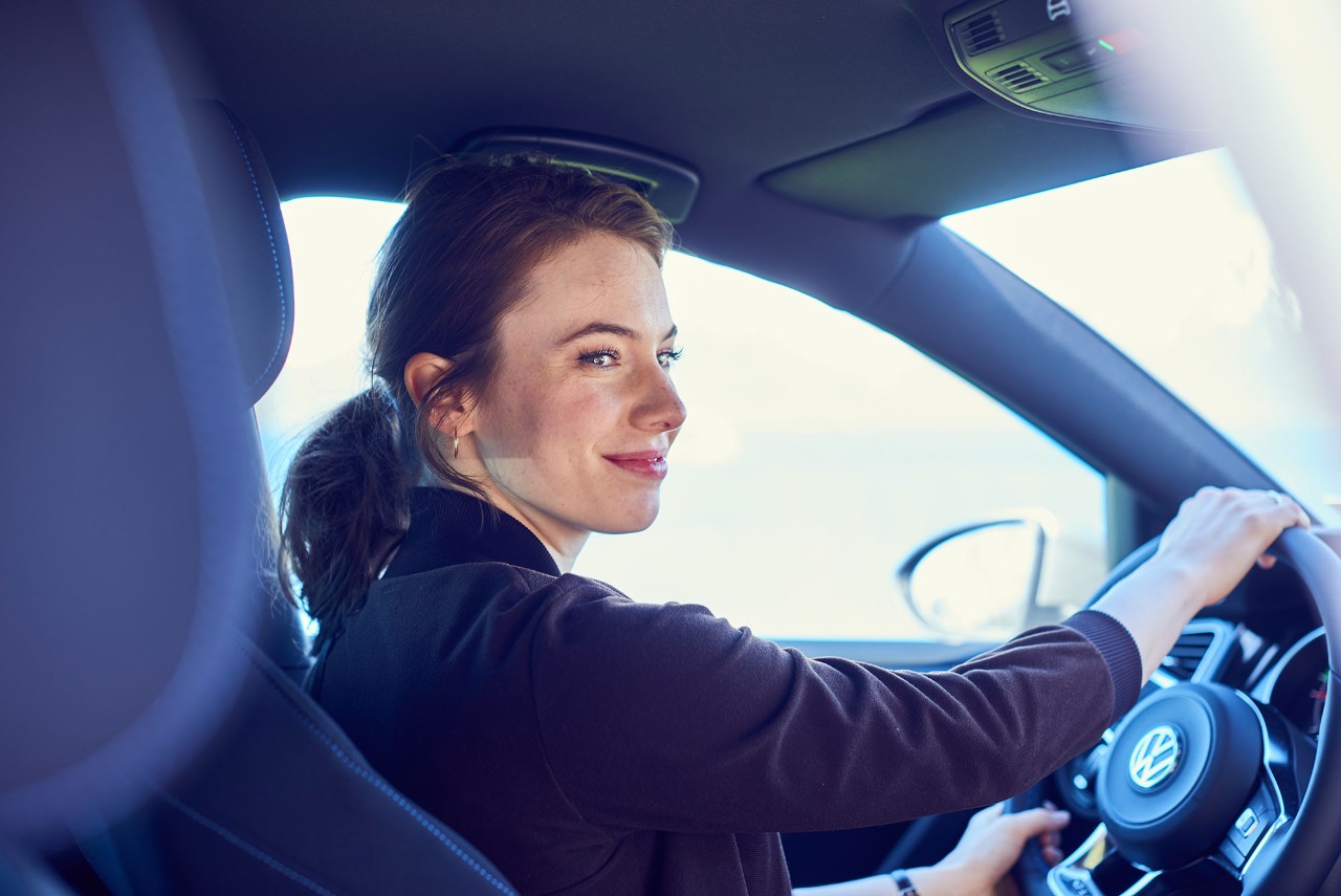 smilende dame med elbil-forsikring ser ut av vinduet i bilen sin