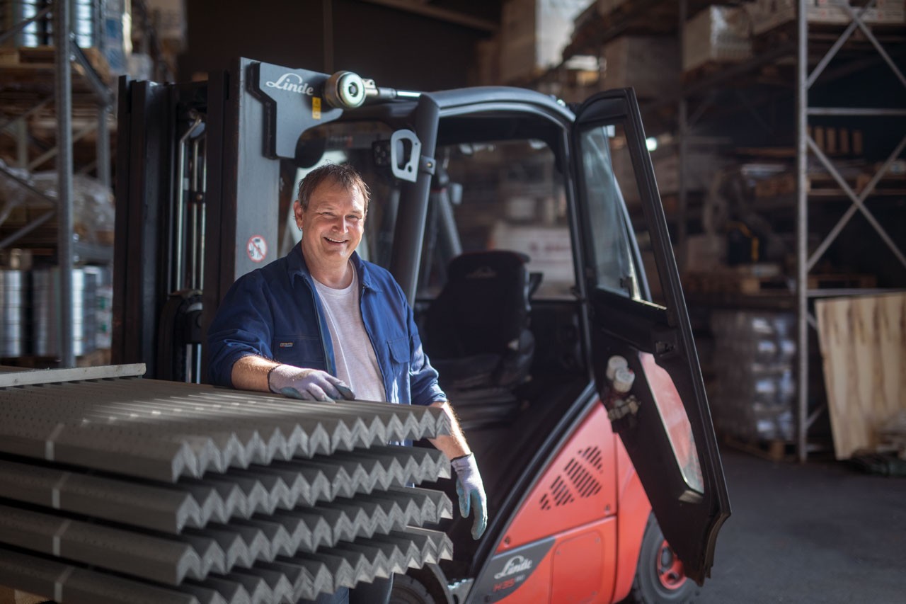 smilende mann ved trucken sin i en speditørbedrift sitt lagerbygg