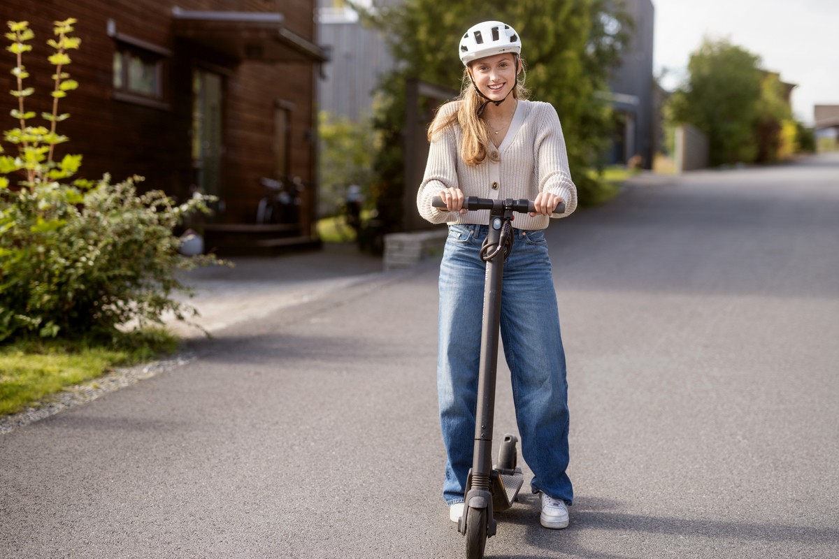 glad jente i gata som har forsikret sin el-sparkesykkel