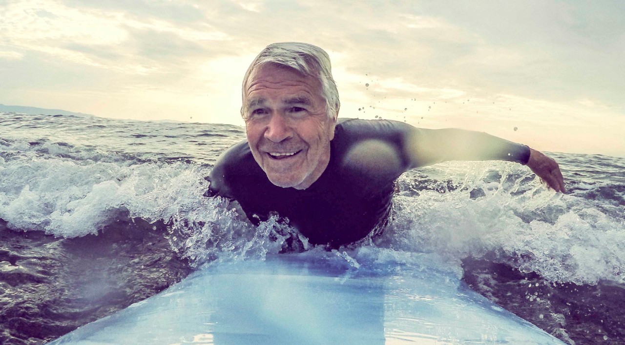 Smilende eldre mann på surfebrett